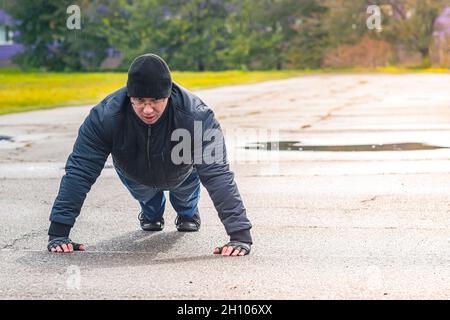 A man performs a classic pectoral exercise outdoors in the rain in the fall. The athlete does push-ups to maintain muscle tone Stock Photo