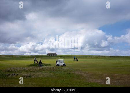 Hafnarfjordur, Iceland - May 31, 2021: Golf players with wheel push carts, and riding an electric golf cart, on a green golf field, on cloudy day. Stock Photo
