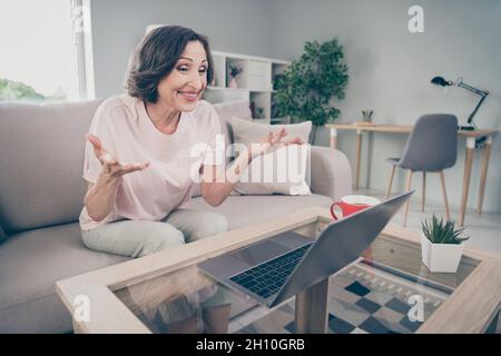 Photo portrait senior woman sitting on sofa working on computer talking on web camera online at home Stock Photo
