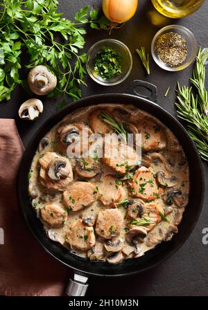 Pork medallions with mushroom gravy in cast iron pan over dark stone background. Top view, flat lay Stock Photo