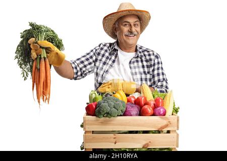 Smiling mature farmer holding broccoli and standing behind a crate with ...