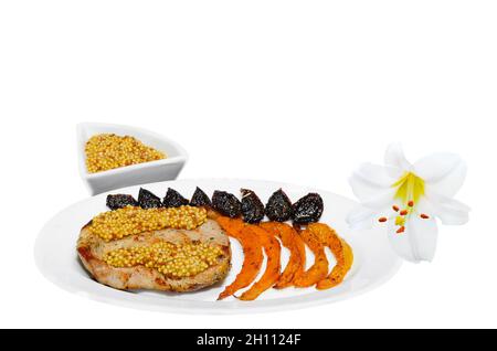 Roast pork on a plate with French mustard, pumpkin and dried spicy plum. White background, selective focus Stock Photo