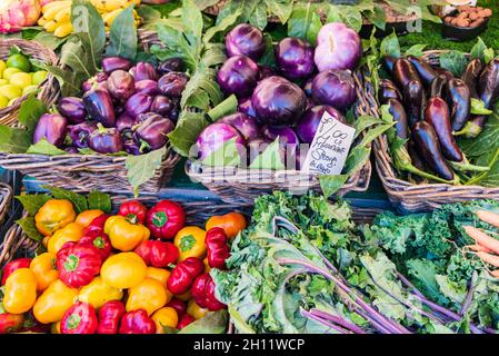 Eggplants at the vegetable market stall. Various colourful vegetables packed in wicker baskets and a price tag of 4 euros. Stock Photo