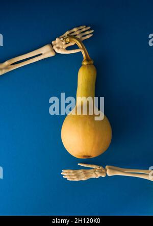 Vertical shot of a ripe squash with a tiny skeleton hand and a red cup ...