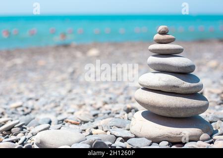 Round stones are stacked on top of each other in a pyramid on the seashore on a sunny day. Balance concept. Copy space. Stock Photo