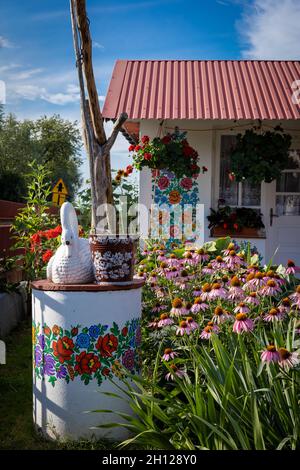 Zalipie, Poland - August 1, 2021: A white well painted in colorful floral pattern, a bucket and a swan statue on top. Pink flowers in the garden. Stock Photo