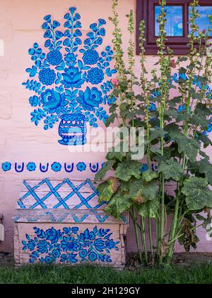 Zalipie, Poland - August 1, 2021: A colorful floral pattern, painted on a white wooden wall. Hollyhock flowers in front of the house. Stock Photo