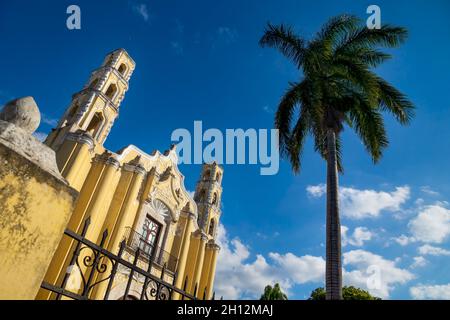 Sunlit facade of the colonial church 'San Juan Bautista' with palm tree on blue sky in the historic center of Merida, Yucatan, Mexico Stock Photo