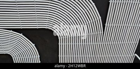 Electrical cables and pipes on house concrete ceiling, background. Modern plastic hoses and conduits with wires in room. Lines of pvc wiring tubes aft Stock Photo