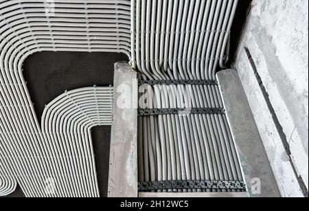 Electrical cables and pipes on house concrete wall and ceiling. Modern plastic hoses and conduits with wires in room. Lines of pvc wiring tubes after Stock Photo