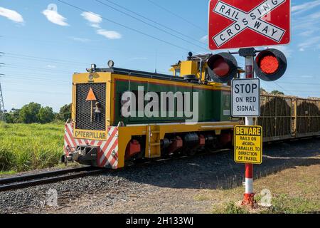 Mackay, Queensland, Australia - October 2021: Train engine hauling filled chopped sugar cane past crossing signage on its way to the mill to be crushe Stock Photo