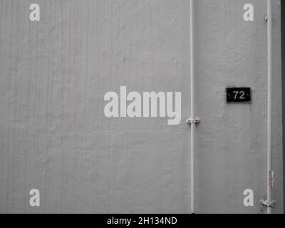 White painted copper pipes and number plate against white wall Stock Photo