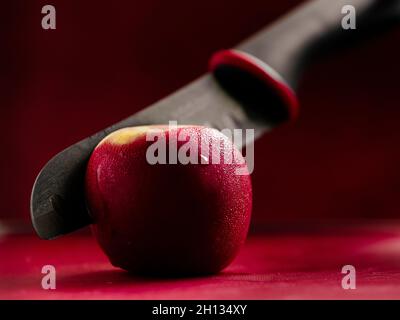 Black ceramic knife cutting into red apple on chopping board Stock Photo