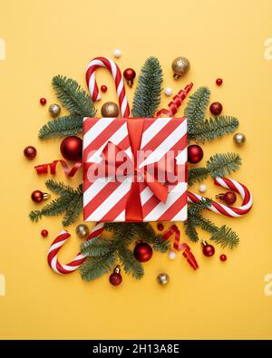 Christmas card with gift box, candy cane, Christmas balls, and fir tree branches on yellow background Stock Photo
