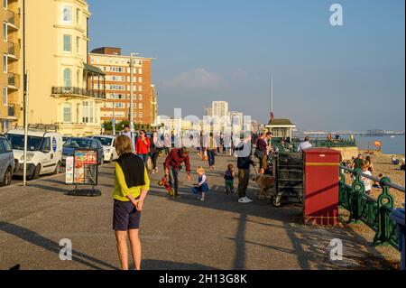 People strolling on Hove promenade in glowing October afternoon sunshine with view to Brighton in the background. East Sussex, England. Stock Photo