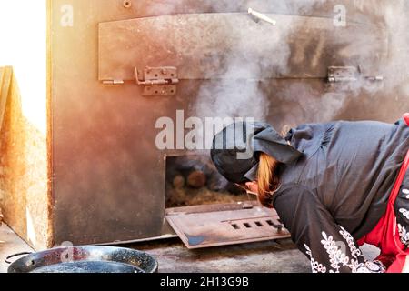 Avila, Spain - September 04, 2021: Woman cook in black suit preparing the wood oven for cooking. Healthy food concept Stock Photo