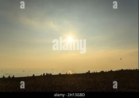 Loads of people sitting on the beach in silhouette against the sea in glowing October afternoon sunshine, Hove, East Sussex, England. Stock Photo