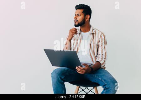 Portrait of business Indian man using laptop computer, looking side and smiling, standing isolated on white background Stock Photo
