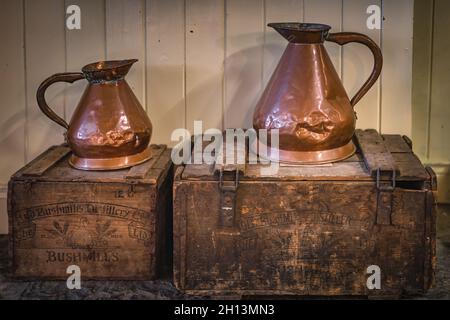 Bushmills, Northern Ireland, Aug 2019 Vintage battered copper jugs standing on wooden crates with Bushmills whiskey bandings Stock Photo