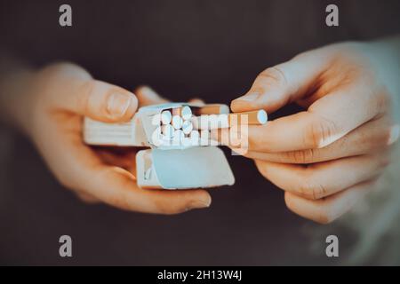 A man holds an open pack of cigarettes in his hands and takes a cigarette out of it to light it. Nicotine addiction. The habit of smoking. Stock Photo