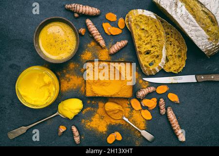Turmeric powder, root, ghee, bread and golden milk on a slate background Stock Photo