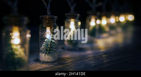 Christmas decoration electric garland with little Christmas tree inside warm-toned lights covered on the wooden board table. Christmas mood wide-open Stock Photo