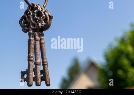 Three old vintage antique rust keys hang in the foreground against a blue sky. Stock Photo