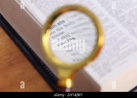 Looking up definition of Vaccine in Longman's Dictionary of Contemporary English, magnifying glass zooming on word in book Stock Photo
