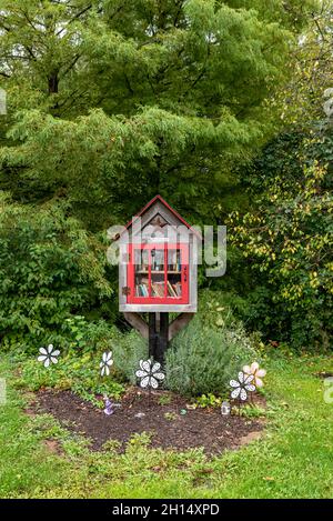 A decorative Little Free Library box stocked with books surrounded by lush green grass and foliage in a neighborhood in Indianapolis, Indiana, USA. Stock Photo