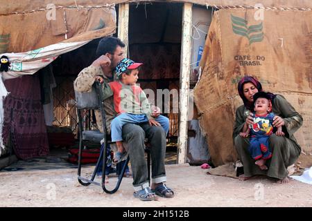 Outside the tent where they live, Abu Mohammad, 33, with his son Mohammad, 4, and his wife Saada, 29, who is trying to pacify two year old Adnan. Sahnaya, Syria. September 5, 2009. Stock Photo