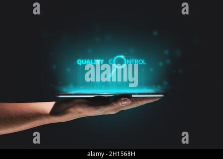 Quality control concept in production and business. A hand holds a tablet with a hologram above it. Stock Photo