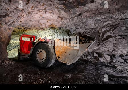 An underground loading machine carries a full bucket of ore. Special low-profile equipment for underground work Stock Photo