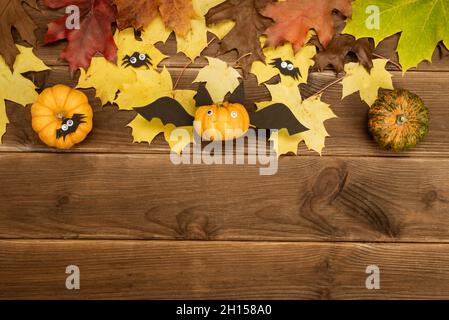 Autumn decor of pumpkin and yellow maple leaves on a wooden background with copy space. DIY pumpkin craft in the shape of a bat. Halloween decor. Stock Photo