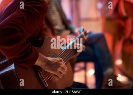Close-up of man sitting on chair and learning to play guitar during lesson Stock Photo
