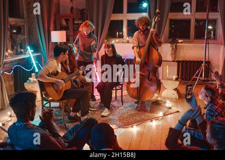 Young people playing musical instruments and singing while gathering together in music studio Stock Photo