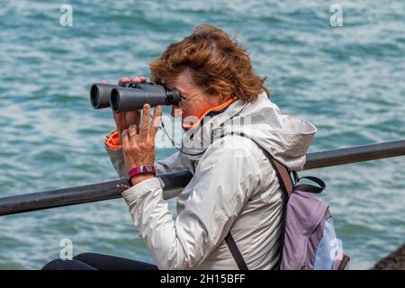 female looking through a large pair of binoculars watching the yachts at the annual cowes week yachting and sailing regatta on the isle of wight uk. Stock Photo
