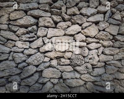 Irregular stone masonry wall background. Old limestone rocks of different size and shapes stacked carefully. Detailed texture of construction element. Stock Photo