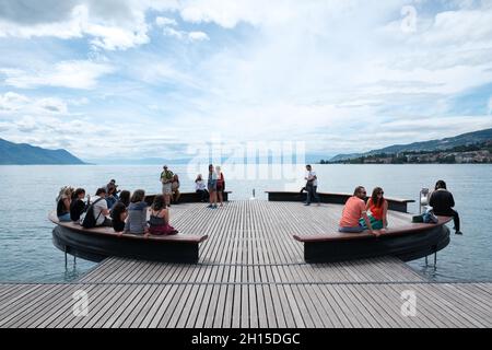 Tourists relaxing on the circular Platform Sur Mer looks out over Lake Geneva right next to statue of Freddie Mercury in Montreux Riviera, Switzerland Stock Photo