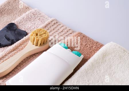 Lifting cream in tube with massage roller nozzle close-up, brush made of natural bristles and gouache made of natural stone for a stack of towels Stock Photo