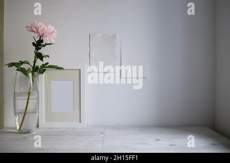 Scandinavian style. Interior Design. Large pink chrysanthemum in a long glass vase. Photo frame. Two blank sheets of paper on the wall. Empty space fo Stock Photo