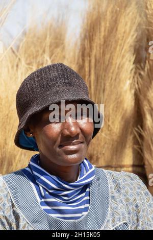 African woman in the village carrying grass used to thatch roofs Stock Photo