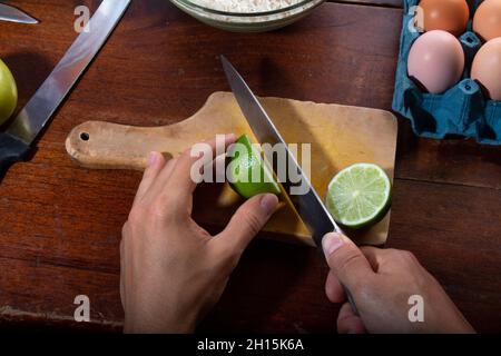 Hands cutting lemon with knife on wooden board. Home cooking concept. Stock Photo