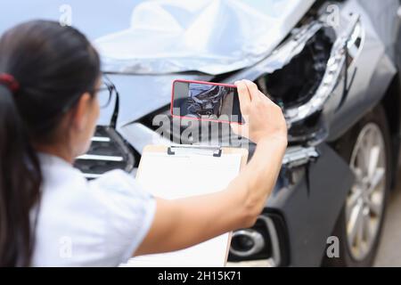 Insurance agent takes pictures of damage to car after accident on smartphone Stock Photo