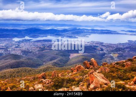 Aerial view over Hobart city from lookout of Mt Wellington at the level with clouds - rough terrain blown by winds. Stock Photo