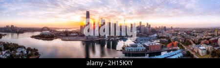 WIde aerial panorma at sunrise over CIty of Sydney with CBD towers hiding the rising sun on shores of Sydney harbour and major architecture landmarks. Stock Photo