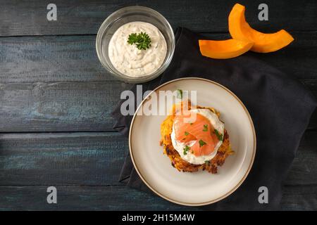 Smoked salmon with a fresh dip on fritters or pancakes from red kuri squash and potatoes, festive autumn snack for Thanksgiving and Halloween on a dar Stock Photo