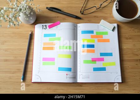 Open diary or appointment calendar with a lot of colorful sticky notes on a wooden desk with coffee pens and glasses, time management concept, copy sp Stock Photo