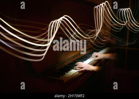 Light painting in the form of curved stave lines above hands playing on an old piano, waves of music, dark background with copy space, motion blur, se Stock Photo