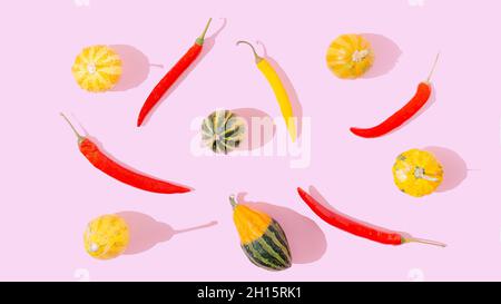 A pattern made of yellow and red hot chili peppers and yellow and green pumpkin on pastel pink background. Happy and healthy autumn food Stock Photo