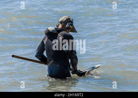 A man with a special device and equipment metal detector looking for lost jewelry and gold in sea water near the beach. Stock Photo